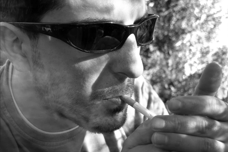 black and white pograph of man wearing sunglasses smoking a cigarette