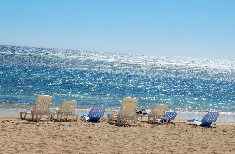 many empty chairs set on the sand near a body of water