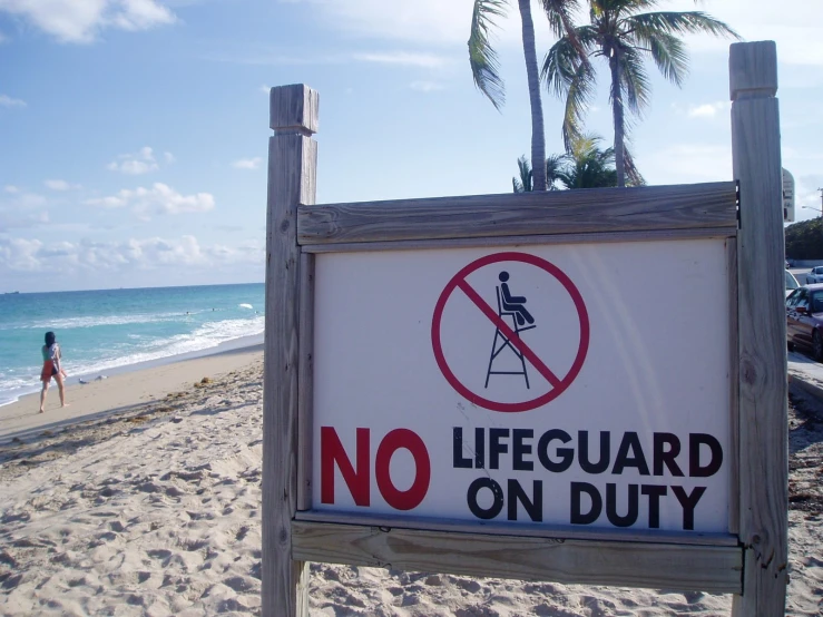 sign on wooden post on sandy beach with woman on water