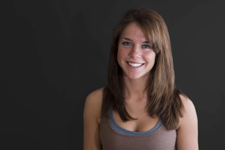 a woman with dark eyes smiles while wearing grey shirt