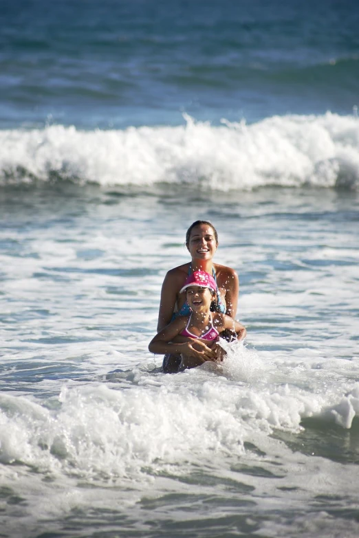 a woman in bikini sitting on a surfboard with her child