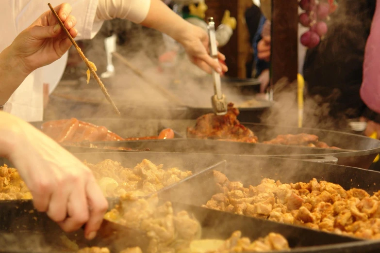 a buffet with tongs, two people and a variety of foods in pans