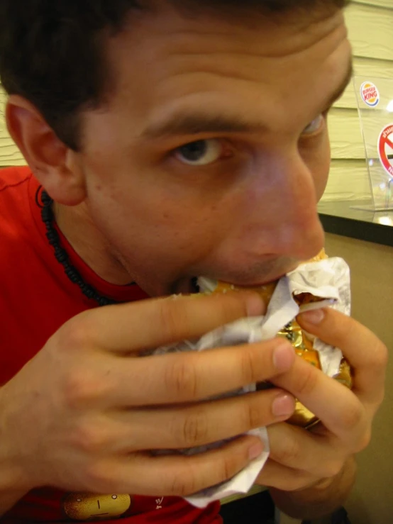 a young man eats a sandwich with foil wrapper around his mouth