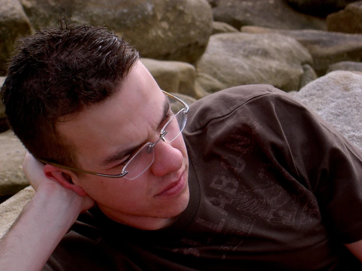a young man laying in the sand wearing glasses
