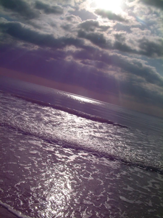 the sky above the ocean and sun shining on the beach