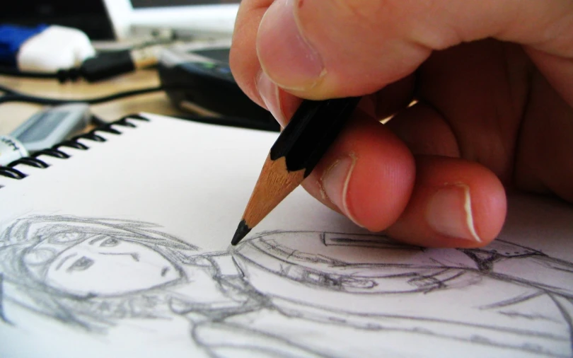 a person drawing with a pencil in a notebook