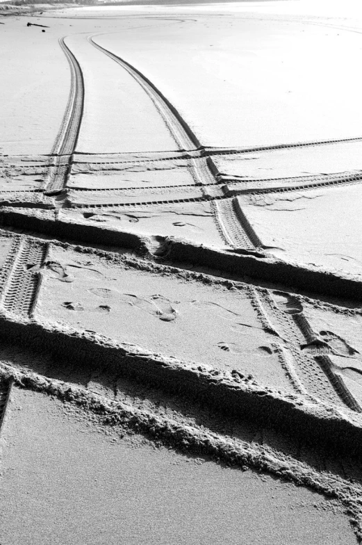 a black and white image of a dirt road with one tire and tire tracks leading into the distance