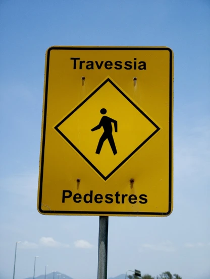 a yellow pedestrian sign is standing in front of a hill