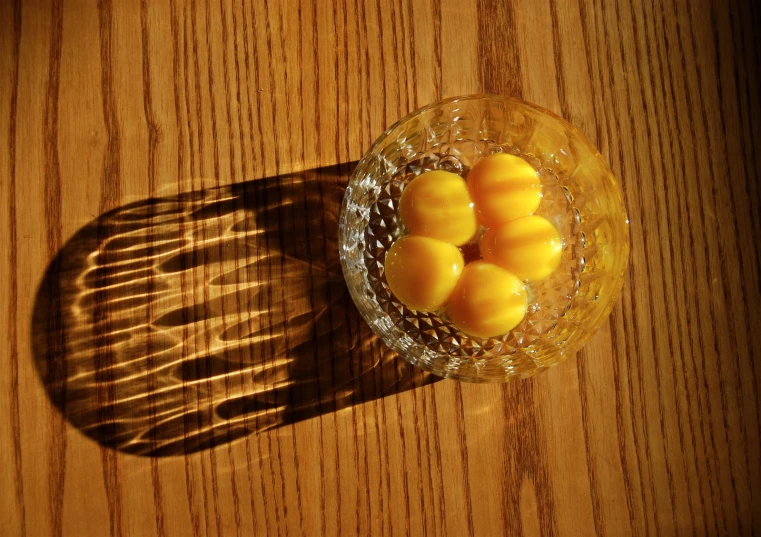 a glass bowl filled with yellow mangoes on top of a wooden table