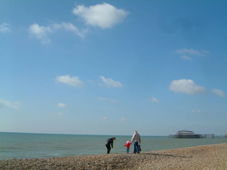 two adults and a child standing on a beach looking at the ocean