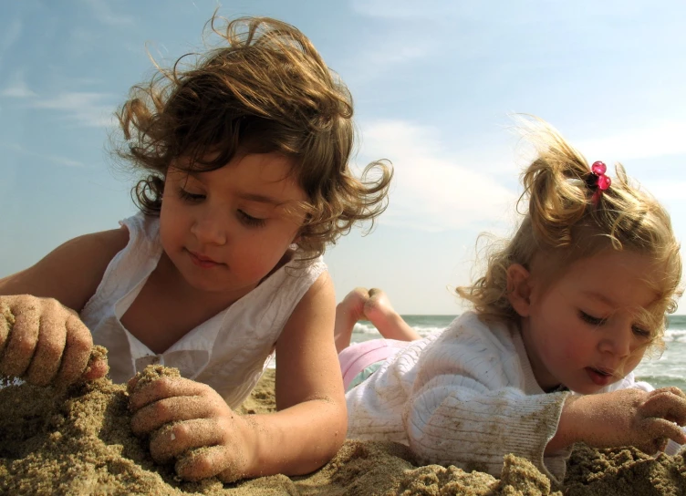 two children are playing in the sand at the beach