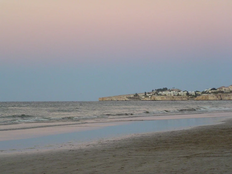 an ocean beach and town near water at sunset