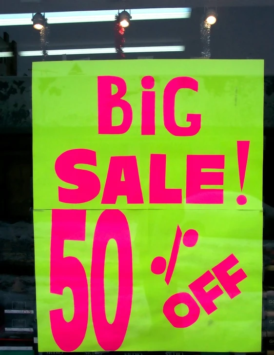 a green sign advertising big sale with neon red lettering on it