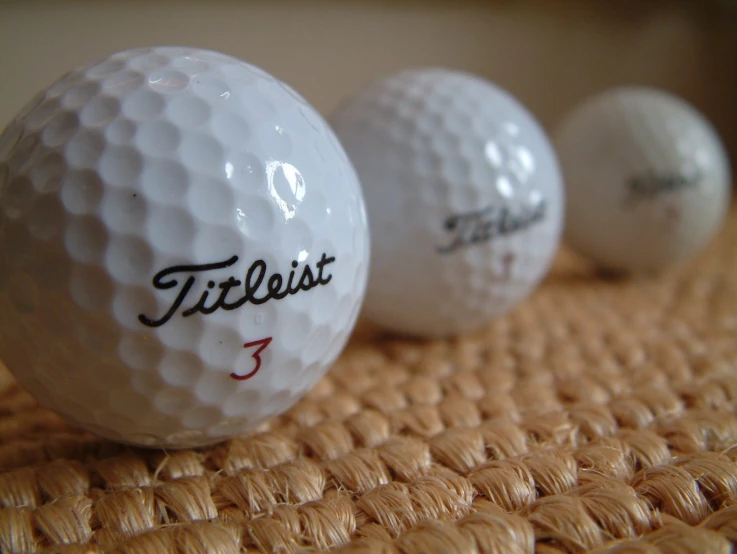 three golf balls and their size on a woven mat