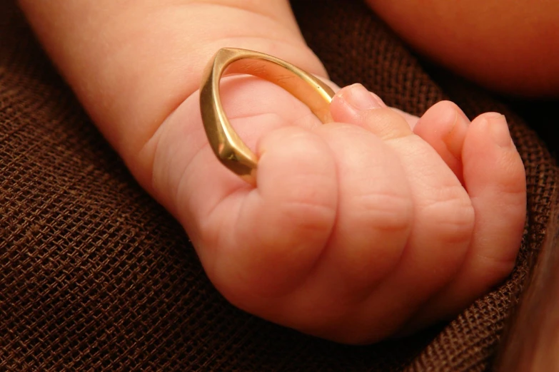 a baby is holding it's hand in a gold ring