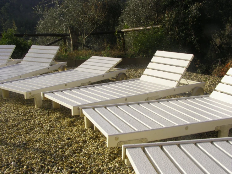 four empty lounge chairs sitting on gravel by trees