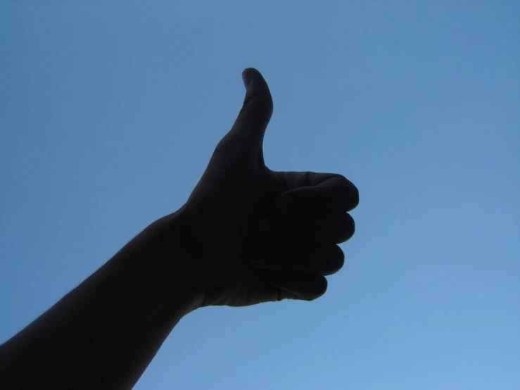 a hand gives the thumbs up sign against a blue sky