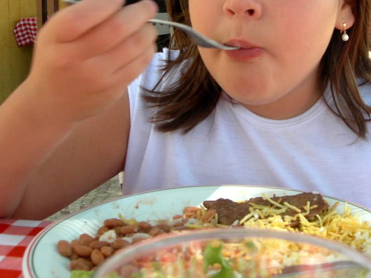 a little girl eating a bowl of beans, rice and salad