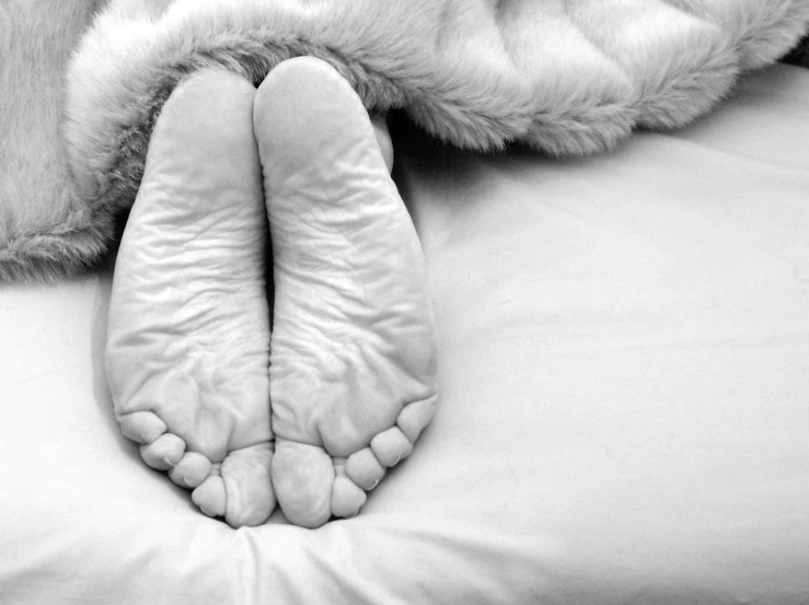 the top half of an unmade bed with the feet of a person and a blanket over them