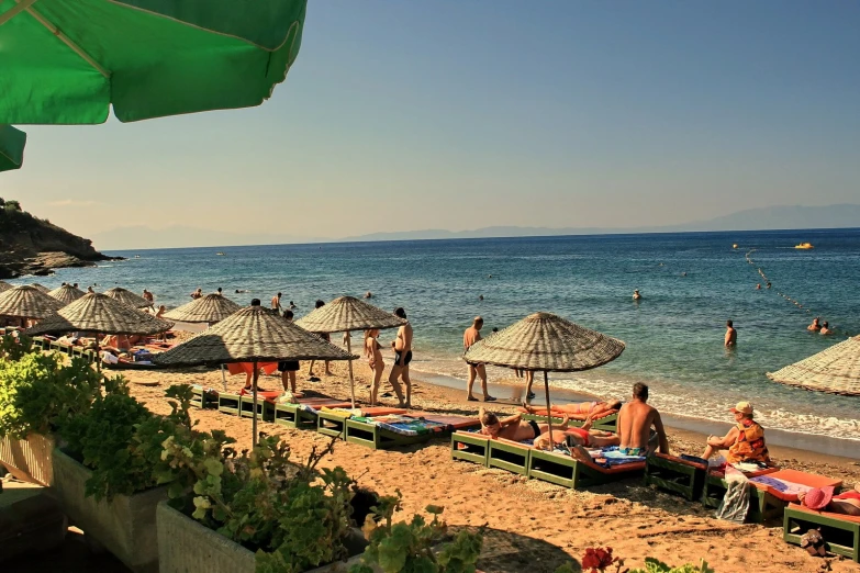 a beach with umbrellas, sand chairs and people in the water