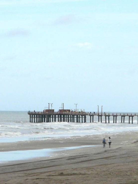 people walk along the beach as an ocean and pier sits in the background