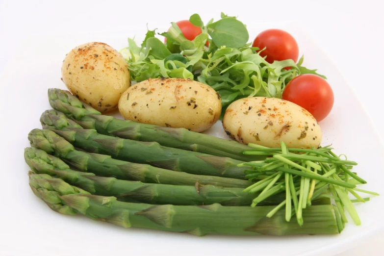 a white plate topped with asparagus, potatoes and fresh salad