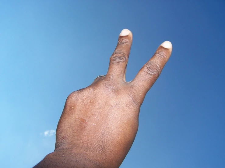 a hand holding up a white ballon against a blue sky