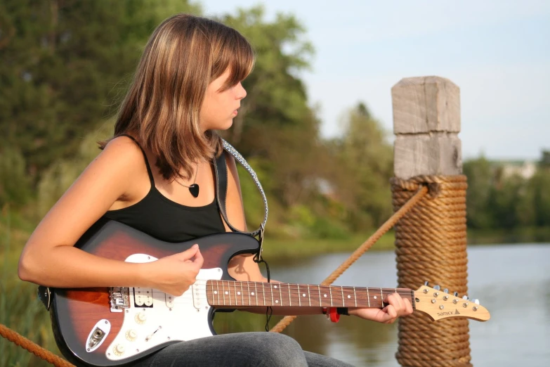 a beautiful young woman holding a guitar next to a body of water