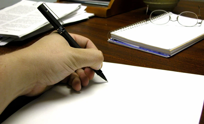 a person is holding a black pen with a paper and book