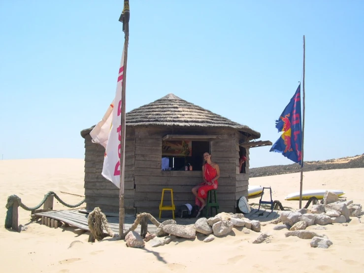 a hut on the beach with flags flying next to it