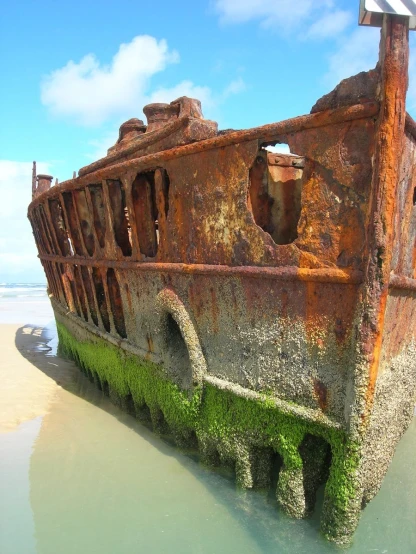 old boat, overgrown with grass, in shallow area next to beach