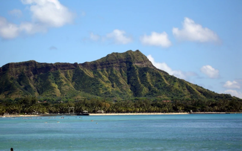 a hill rises high above the blue ocean and beach