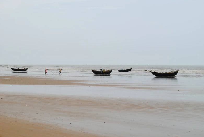 people walk along the shore of a beach near fishing boats