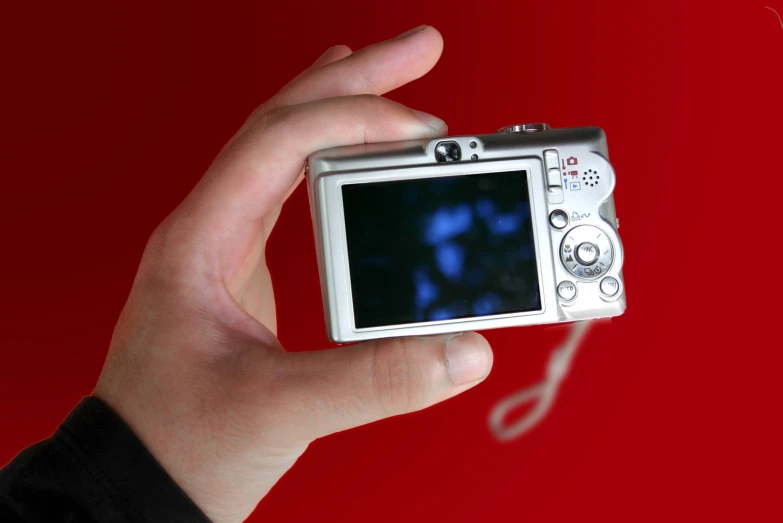 a hand holding a small camera in front of a red wall