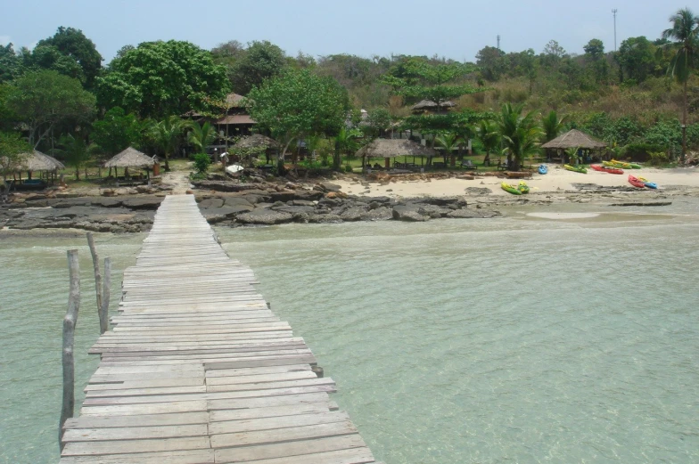 a wooden dock crossing into the ocean next to beach