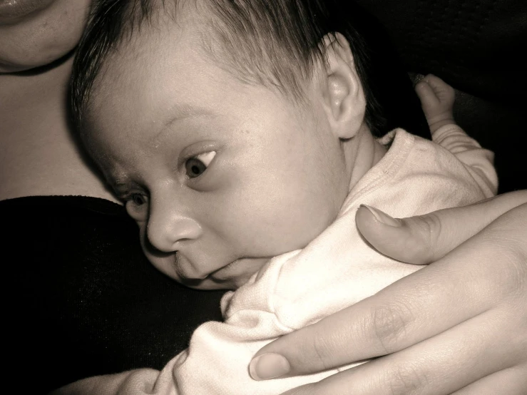 a baby wearing a white shirt laying on top of a woman