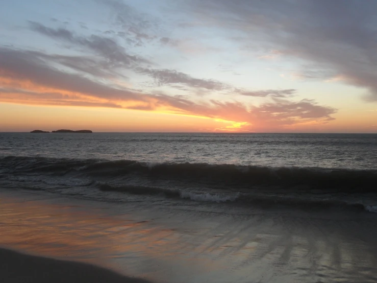 the sun sets on a beach with the ocean in front