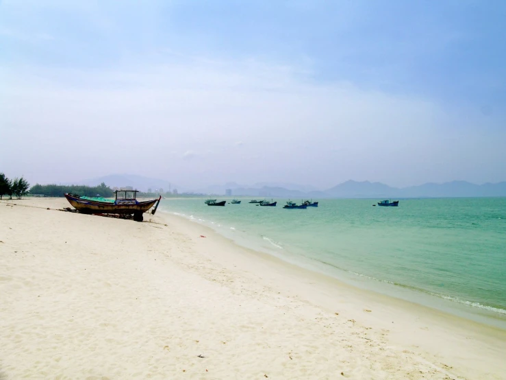 a white sandy beach that is partially shaded with boats