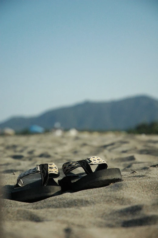 two black sandals sitting on top of a sandy beach