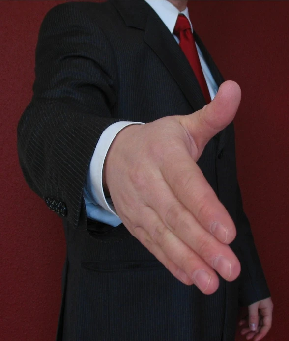 a man wearing a suit and red tie pointing with both hands