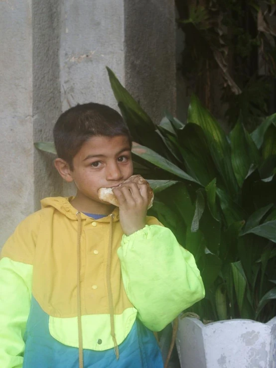 the child is wearing a yellow and blue jacket and eating soing