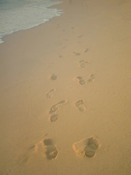 footprints are in the sand near a man's surfboard