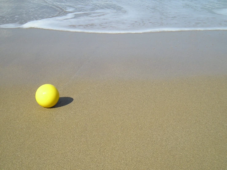 a yellow ball is on the sandy beach
