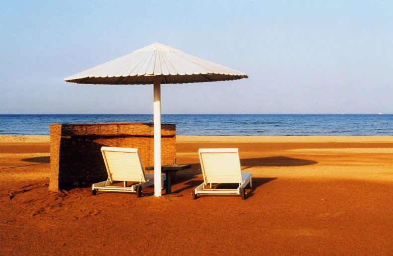 two beach chairs and an umbrella on the sandy beach