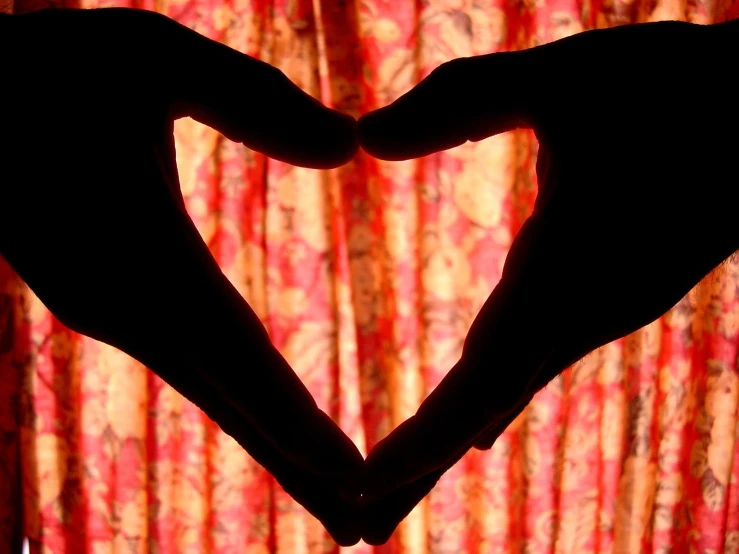 two hands make a heart shape against a curtain