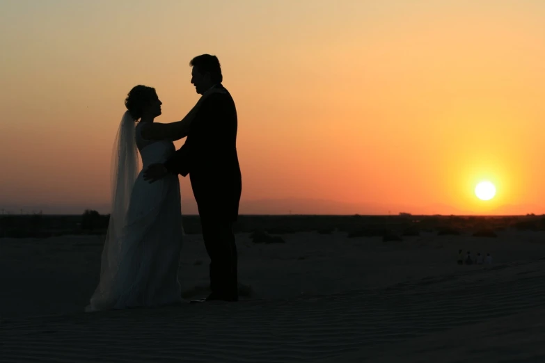 a man and a woman standing in the desert at sunset