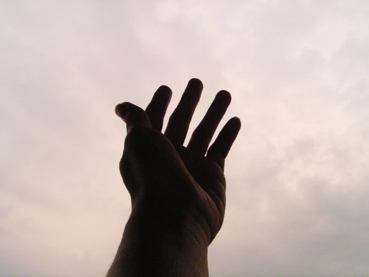 a hand reaching up to a cloudy sky