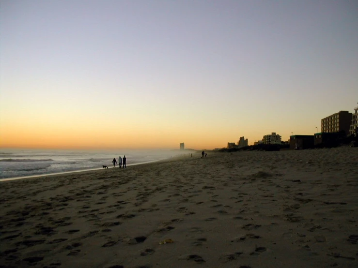 a beach with people walking around and buildings in the background