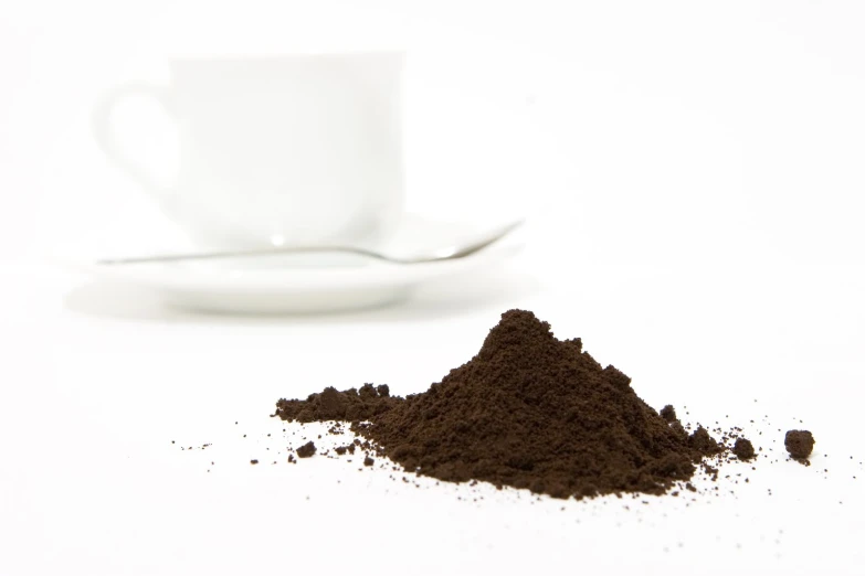 a bowl full of dark brown powder next to a coffee cup