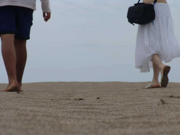 a pair of people with hand bags walking on a sandy beach